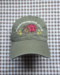 An olive green baseball cap with an embroidered ladybug and the words 'OVERTHINKING CLUB' on the front, displayed on a brown and white checkered fabric background.